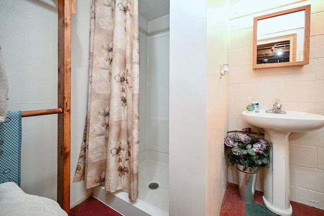 full bath featuring a stall shower, concrete block wall, and a sink