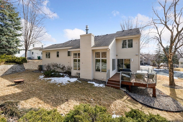 back of house with a chimney, a deck, and a shingled roof