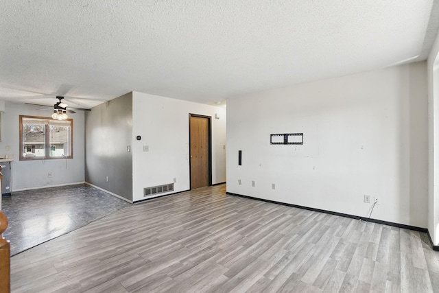 unfurnished living room featuring a ceiling fan, wood finished floors, visible vents, and a textured ceiling