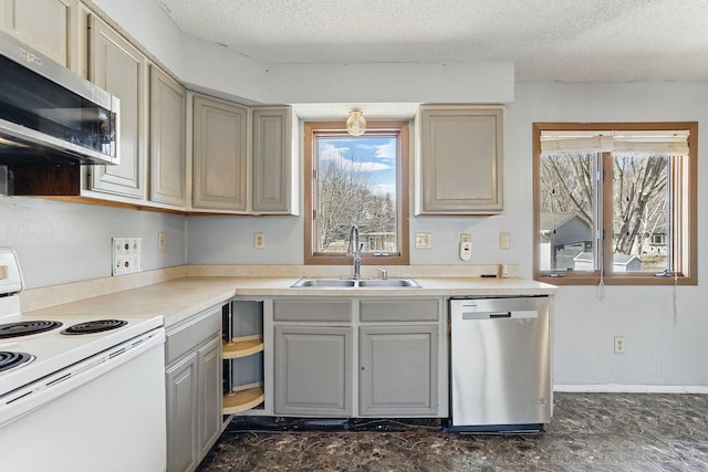 kitchen with appliances with stainless steel finishes, a textured ceiling, gray cabinetry, and a sink