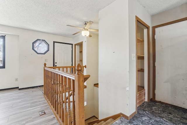 hallway with light wood-style floors, an upstairs landing, baseboards, and a textured ceiling