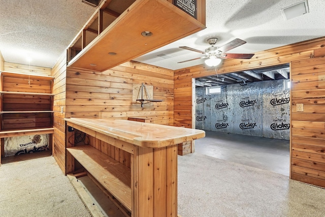 interior space featuring wood walls, a textured ceiling, a ceiling fan, and a bar