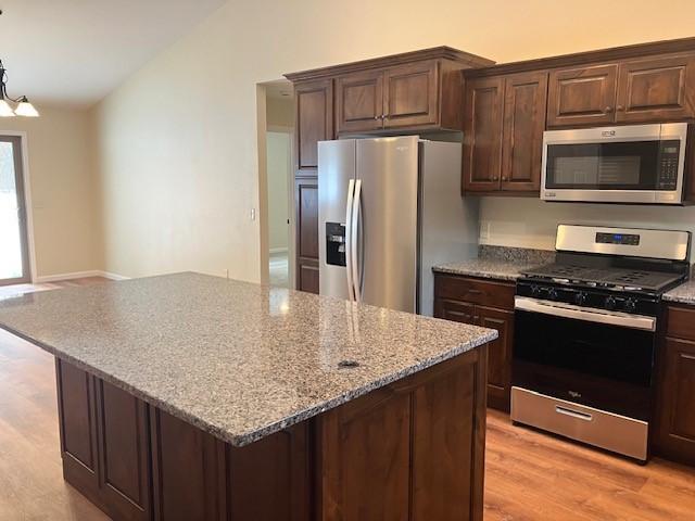 kitchen with a kitchen island, light stone countertops, dark brown cabinetry, vaulted ceiling, and stainless steel appliances