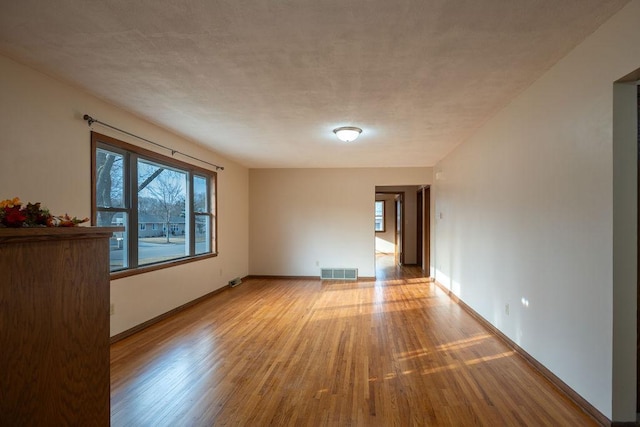 empty room featuring light wood-type flooring, visible vents, and baseboards