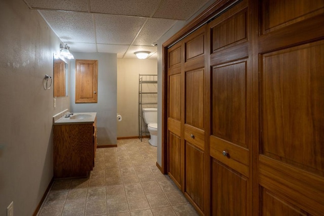 bathroom featuring baseboards, a paneled ceiling, toilet, and vanity