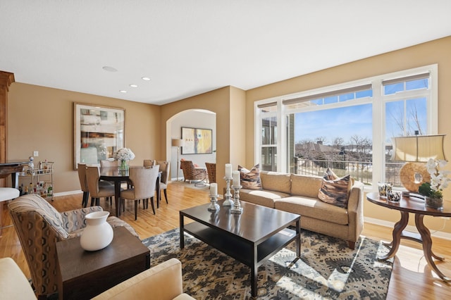 living area featuring light wood-style flooring, recessed lighting, baseboards, and arched walkways