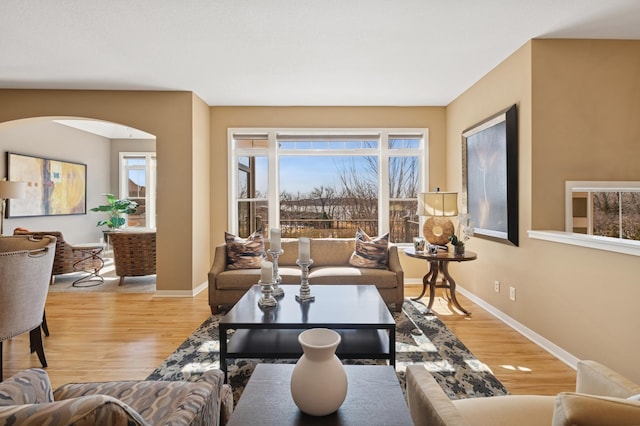 living area with wood finished floors, arched walkways, and baseboards