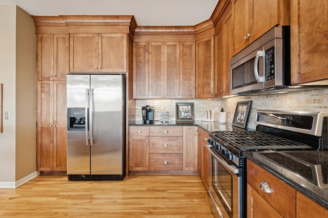 kitchen with dark stone countertops, light wood-style flooring, brown cabinetry, and appliances with stainless steel finishes