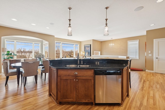 kitchen featuring light wood-style flooring, a kitchen island with sink, a sink, pendant lighting, and dishwasher