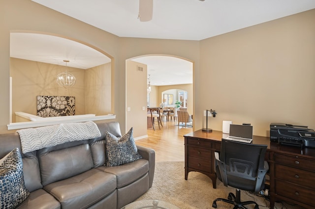 home office featuring light wood-style flooring, ceiling fan with notable chandelier, visible vents, and arched walkways