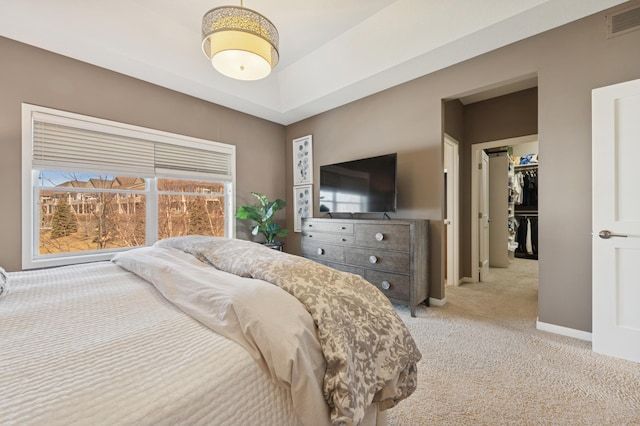 bedroom featuring a spacious closet, visible vents, baseboards, light colored carpet, and a tray ceiling