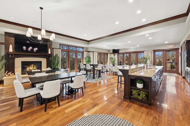 dining space with light wood-style flooring, ornamental molding, french doors, an inviting chandelier, and a fireplace