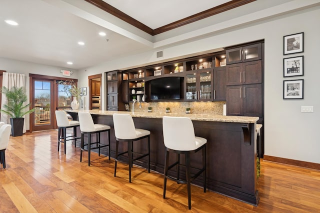 bar featuring tasteful backsplash, crown molding, baseboards, light wood-style flooring, and wet bar