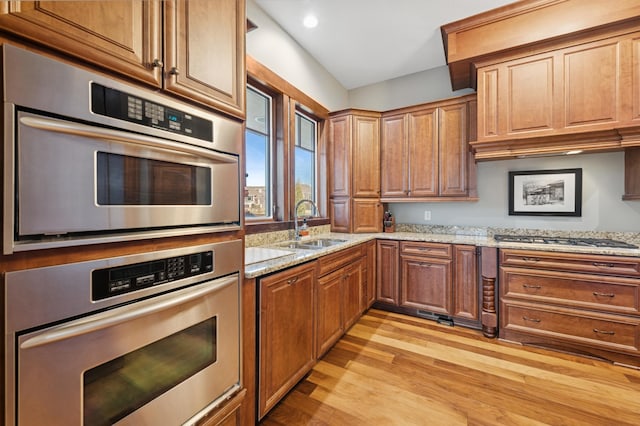 kitchen featuring light stone counters, light wood-style flooring, appliances with stainless steel finishes, and a sink