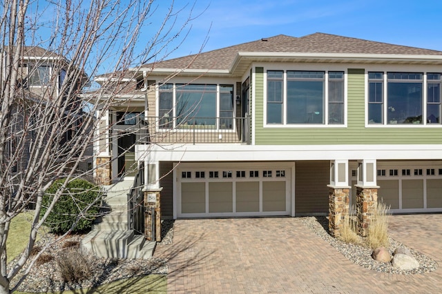 view of front of house with stone siding, driveway, an attached garage, and a shingled roof