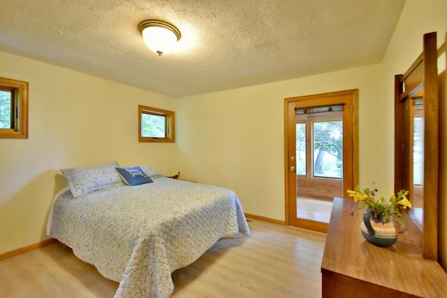 bedroom with light wood finished floors, multiple windows, a textured ceiling, and baseboards