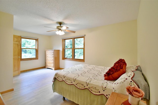 bedroom with baseboards, ceiling fan, a textured ceiling, and light wood-style floors