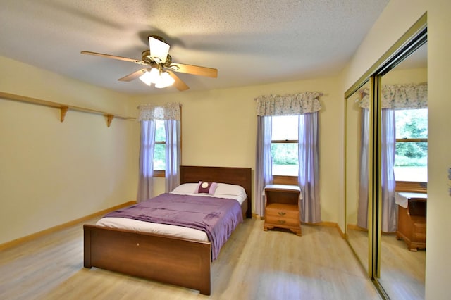 bedroom featuring light wood finished floors, multiple windows, a textured ceiling, and a ceiling fan