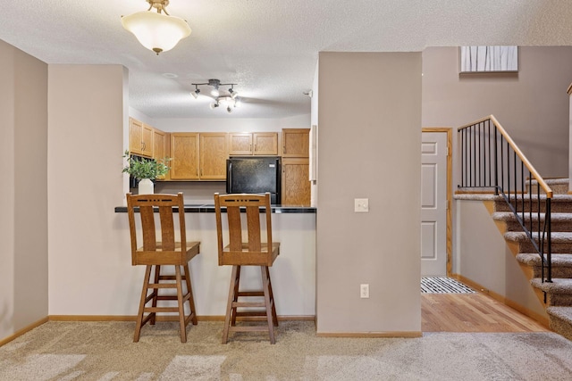 kitchen with light carpet, a kitchen breakfast bar, a textured ceiling, and freestanding refrigerator