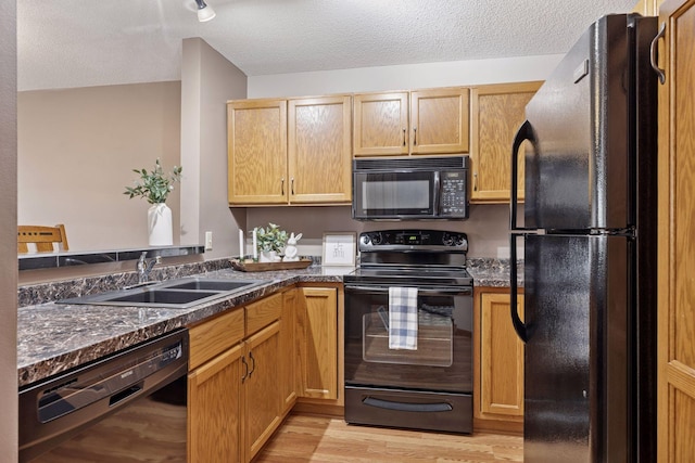 kitchen with light wood-style flooring, a textured ceiling, black appliances, and a sink