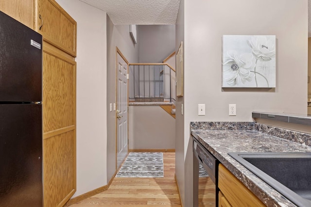 interior space featuring black appliances, a sink, a textured ceiling, light wood-style floors, and baseboards