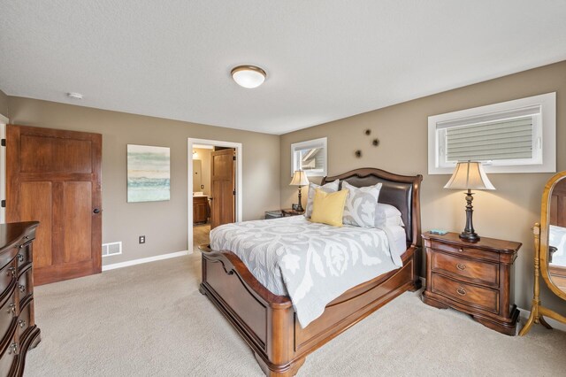 bedroom featuring ensuite bathroom, baseboards, light colored carpet, and visible vents