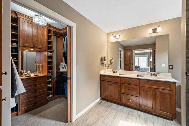 bathroom with a spacious closet, baseboards, a textured ceiling, a sink, and double vanity