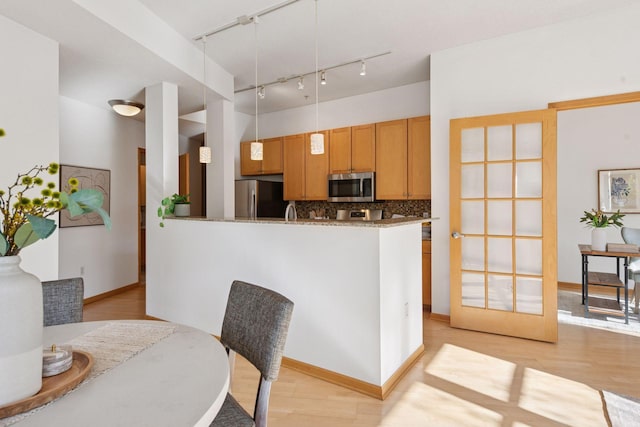 kitchen featuring appliances with stainless steel finishes, rail lighting, decorative light fixtures, decorative backsplash, and light wood-type flooring