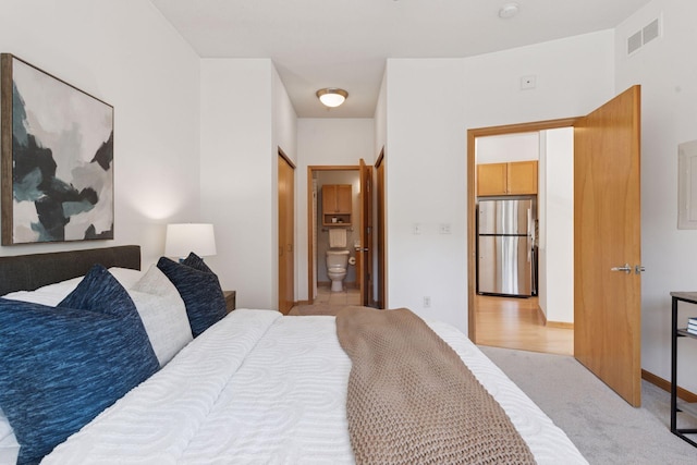bedroom with visible vents, freestanding refrigerator, ensuite bath, and light colored carpet