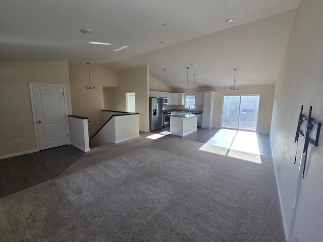 unfurnished living room featuring baseboards, dark carpet, a notable chandelier, high vaulted ceiling, and a sink