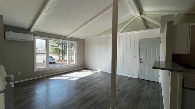 interior space featuring dark wood finished floors, vaulted ceiling with beams, a wall mounted air conditioner, and baseboards