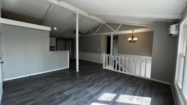 spare room with vaulted ceiling with beams, baseboards, a chandelier, wood finished floors, and a wall mounted AC