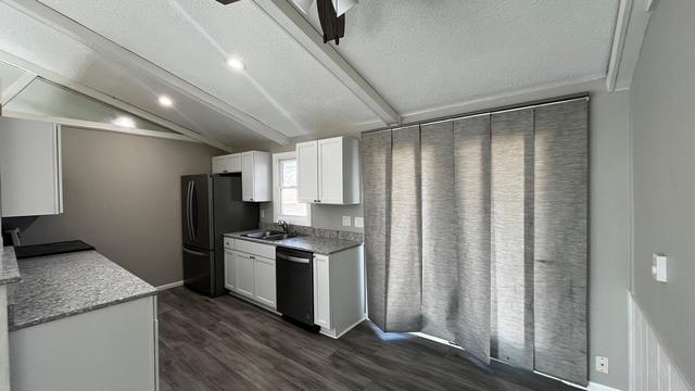 kitchen featuring vaulted ceiling with beams, dark wood-type flooring, dishwashing machine, freestanding refrigerator, and white cabinets