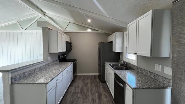 kitchen with a sink, black appliances, vaulted ceiling, dark wood-type flooring, and white cabinetry