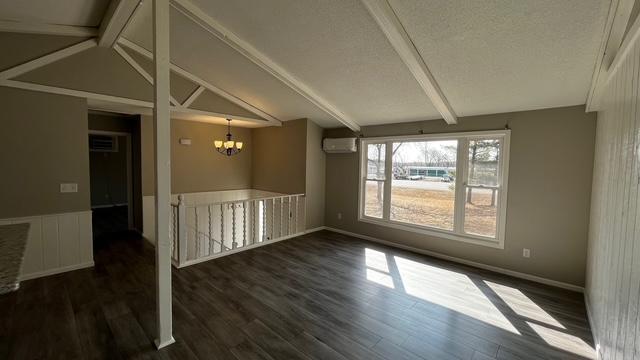 spare room with a wall mounted air conditioner, an inviting chandelier, dark wood-style floors, and vaulted ceiling with beams