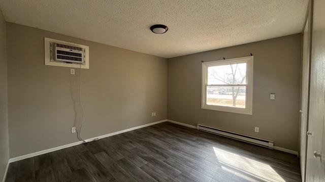 unfurnished room featuring a baseboard radiator, baseboards, a textured ceiling, and dark wood-style floors