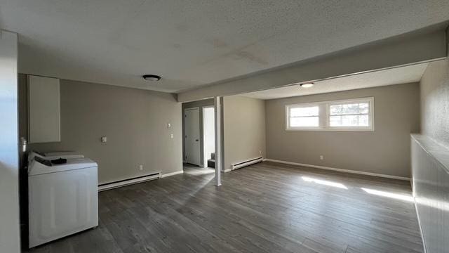 below grade area with dark wood-style floors, baseboards, a baseboard radiator, washer / clothes dryer, and baseboard heating