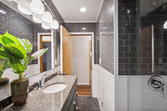 full bath with tiled shower, vanity, and tile walls