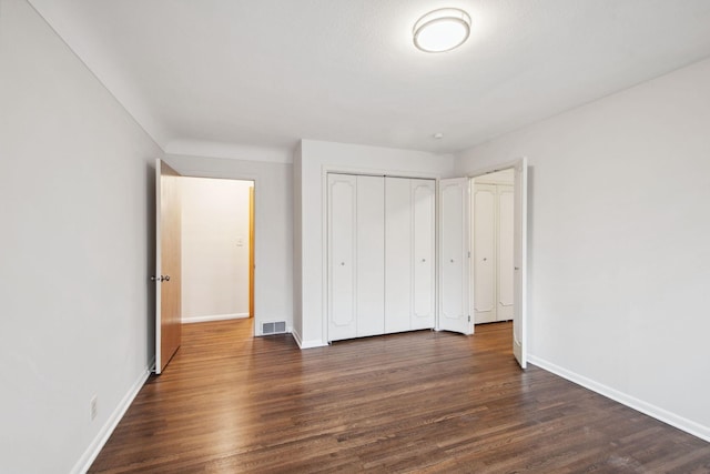 unfurnished bedroom with dark wood finished floors, baseboards, visible vents, and a closet