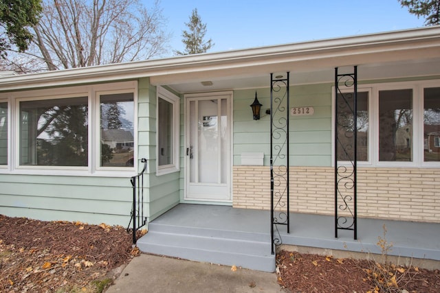 doorway to property featuring covered porch and brick siding