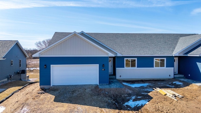 ranch-style house with an attached garage, roof with shingles, and dirt driveway