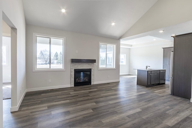 unfurnished living room featuring a wealth of natural light, lofted ceiling, dark wood-style flooring, and a fireplace