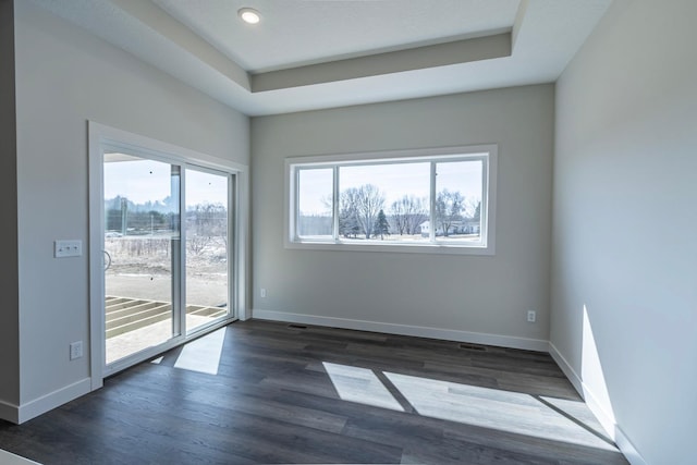 empty room featuring dark wood finished floors, a tray ceiling, and baseboards