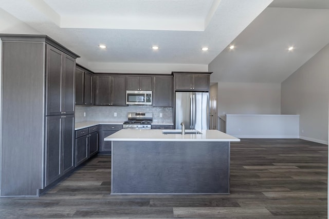 kitchen with backsplash, light countertops, dark wood-style floors, stainless steel appliances, and a kitchen island with sink