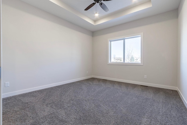 spare room with dark carpet, baseboards, a tray ceiling, and ceiling fan