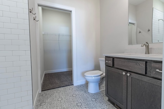 full bathroom featuring a walk in closet, toilet, a shower, baseboards, and vanity