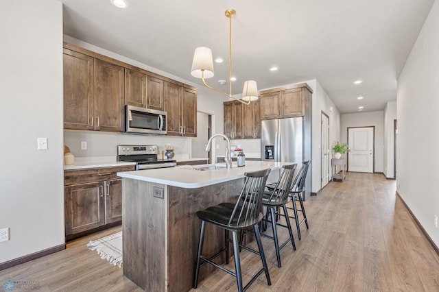 kitchen featuring a sink, stainless steel appliances, a kitchen breakfast bar, and light wood-style flooring