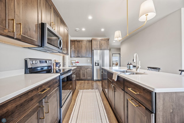 kitchen featuring light wood finished floors, stainless steel appliances, light countertops, and a sink