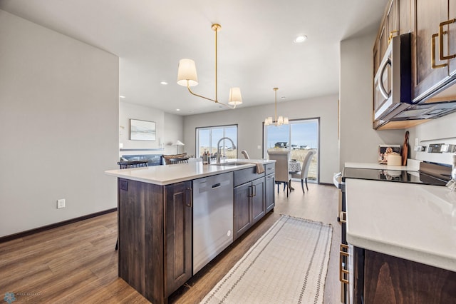 kitchen featuring a kitchen island with sink, a sink, wood finished floors, appliances with stainless steel finishes, and light countertops