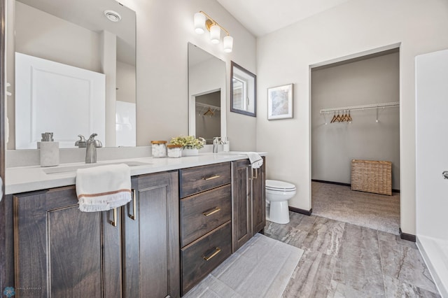 full bathroom featuring a walk in closet, toilet, a sink, double vanity, and baseboards